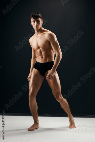 athletic men with a pumped-up muscular body in black shorts posing against a dark background