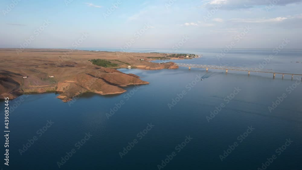 Speedboats sail along the strait. Top view from the drone. Plume on the water. You can see the bridge over the lake, the rocky shore. The water reflects the clouds and the sky. Kapchagai reservoir. Speedboats sail along the strait. Top view from the drone. Plume on the water. You can see the bridge over the lake, the rocky shore. The water reflects the clouds and the sky. Kapchagai reservoir.