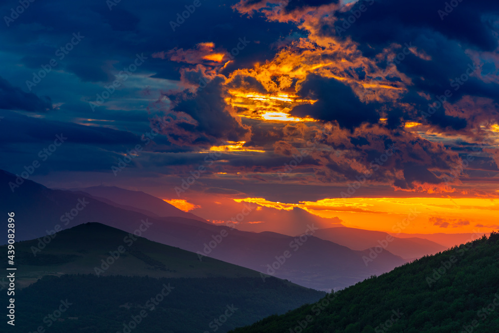 Sunset dramatic sky over mountains landscape in Marche region, Italy. Scenic sunlight beyond storm clouds, distant mountain silhouette, emotional feeling concept.