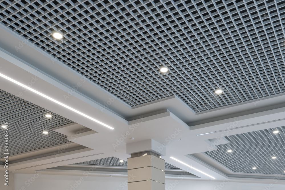 suspended and grid ceiling with halogen spots lamps and drywall construction in empty room in store or house. Stretch ceiling white and complex shape. - obrazy, fototapety, plakaty 