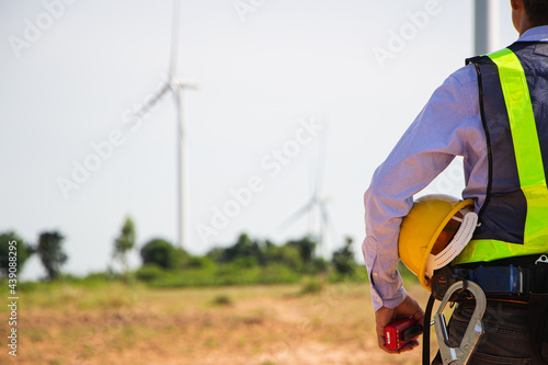 rear view man engineer wearing Personal protective equipment working in wind turbine farm background copy space