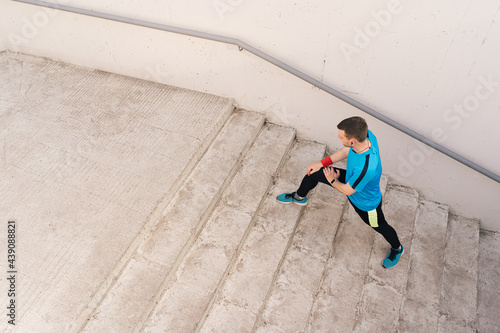 Young man runner getting ready to run stretching legs warm up quad stretch exercise on outdoor staircase