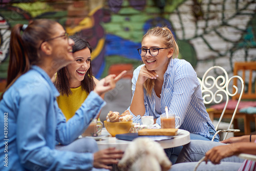 group of young adult female friends talking and laughing in outdoor cafe, drinking coffee