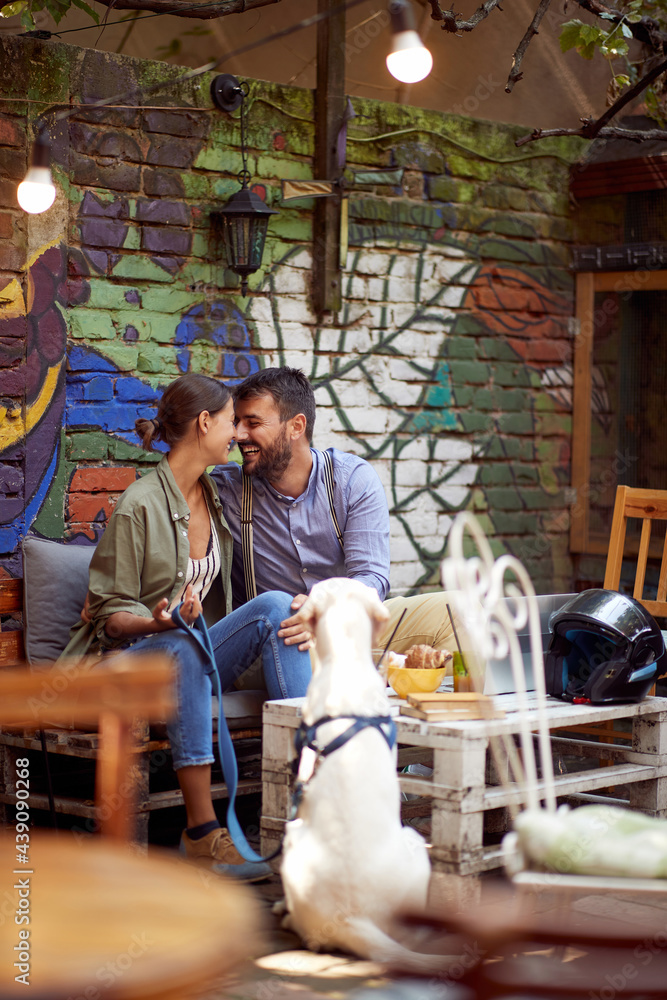young couple cuddling, smiling,  sitting in outdoor cafe with their dog. copy space.