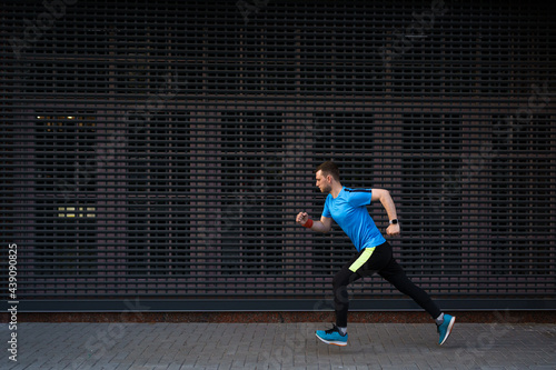 Sport, fitness concept. Sporty man in a blue shirt running outdoors, spring running, attractive Caucasian runner jogs fast over urban gray background