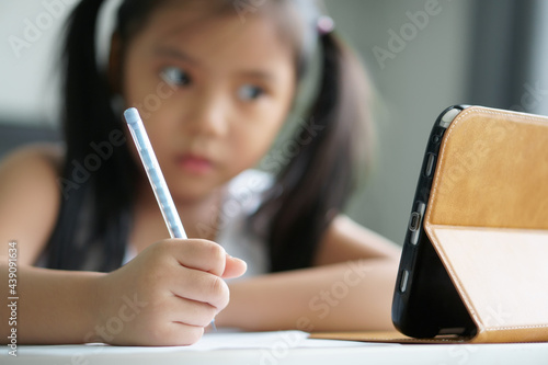 asian child student back to school or kid girl e-learning write note or draw by pencil and read on computer tablet with doing homework to think or people learn from home study online on smartphone pad