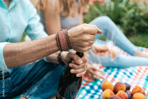Close up man hands opening a sparkling wine while sitting on a blanket with his wife celebrating life, enjoying each other