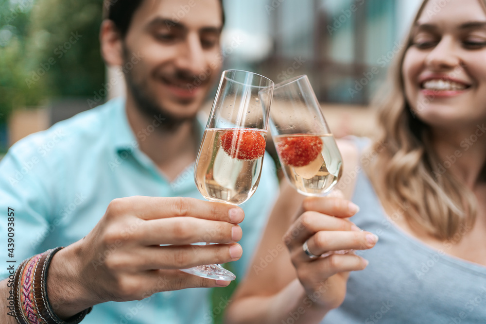 Happy couple portrait clinking two glasses with sparkling wine and strawberries inside with blurred house on background. Celebrating love Happy couple portrait clinking two glasses with sparkling wine and strawberries inside with blurred house on background. Celebrating love