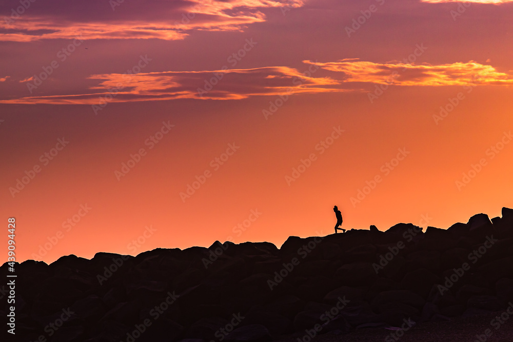 Silhouette photo of a person walking along rocks at sunset