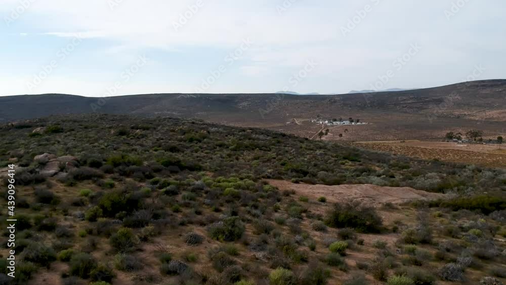 Looking down on a homestead in a semi-arid valley green bushes in the foreground and building in the distance and to the right camera moving right to left Aerial video. Looking down on a homestead in a semi-arid valley green bushes in the foreground and building in the distance and to the right camera moving right to left Aerial video.
