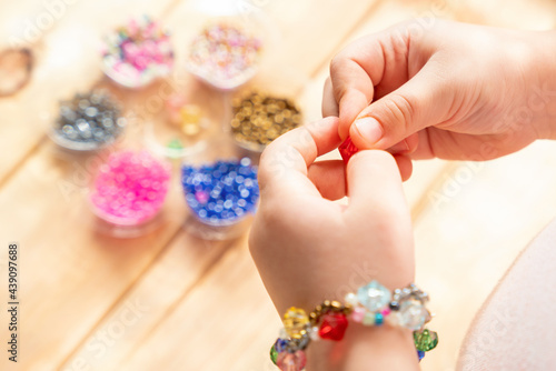 The child makes jewelry with his own hands, stringing colorful beads on a thread