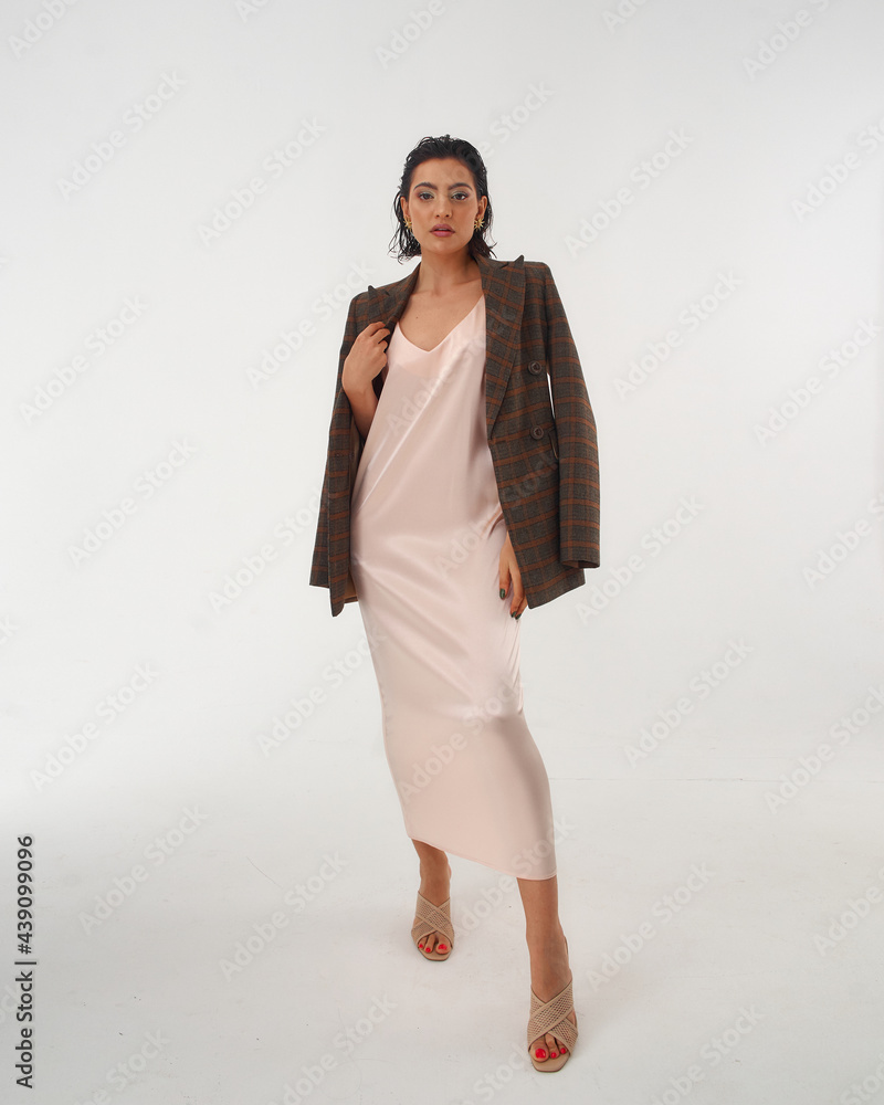 Elegant woman in peach color silk slip dress and brown squared wool blazer standing and posing in studio at white background. Pretty stylish brunete girl with makeup and wet hair full length portrait Elegant woman in peach color silk slip dress and brown squared wool blazer standing and posing in studio at white background. Pretty stylish brunete girl with makeup and wet hair full length portrait