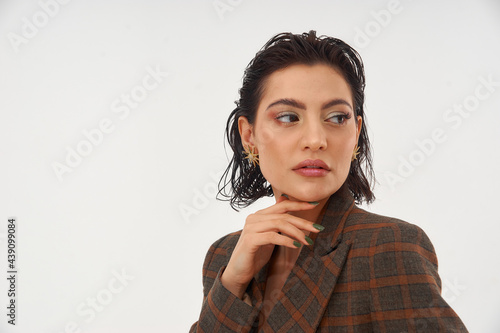 Breast up fashion studio portrait of tanned caucasian woman with brunette wet hair in brown wool squared blazer on grey background. photo