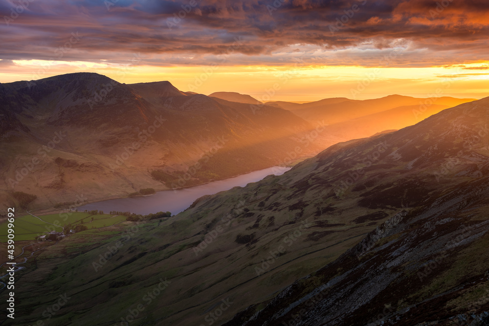 Spectacular Lake District sunset with beautiful glowing rays of light shining onto mountains and valley of Buttermere. Rugged British landscape with dramatic clouds in sky.