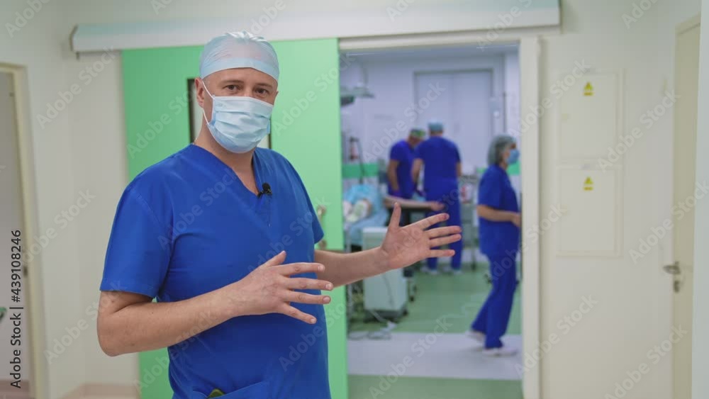 Portrait of a doctor in medical uniform and mask. Plastic surgeon speaking on camera in the hospital hall. Professional surgeon in operating room background. Portrait of a doctor in medical uniform and mask. Plastic surgeon speaking on camera in the hospital hall. Professional surgeon in operating room background.
