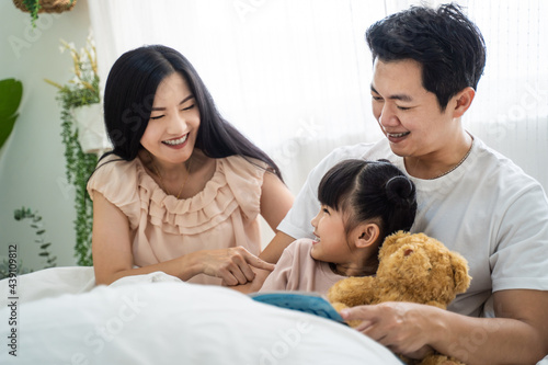 Asian family parent read storytale book to young daughter in bedroom. photo