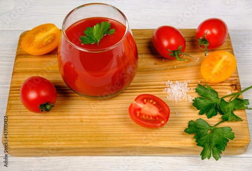 a glass of tomato juice on a cutting board with slices of red and yellow tomatoes
