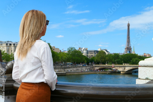 Fototapeta Naklejka Na Ścianę i Meble -  Portrait of a woman with long blond hair, from behind, who contemplates the city. Seine river and Eiffel Tower blurred in the background.