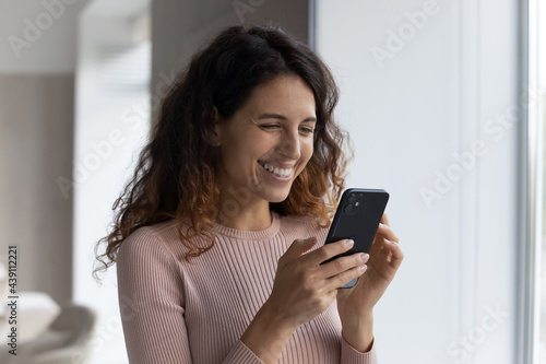 Happy millennial Latino woman hold cellphone look at screen browse wireless internet on gadget. Smiling Hispanic female use smartphone talk speak on video webcam online virtual call on modern device.