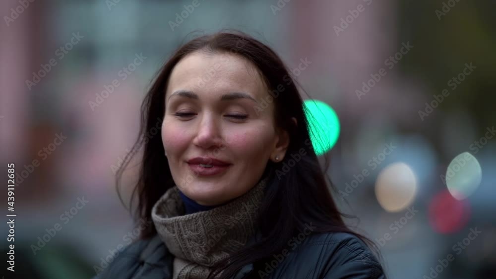 a portrait of a brunette with long hair in a knitted sweater and a dark coat on a cloudy day against the background of city lights is out of focus. she smiles. close-up a portrait of a brunette with long hair in a knitted sweater and a dark coat on a cloudy day against the background of city lights is out of focus. she smiles. close-up