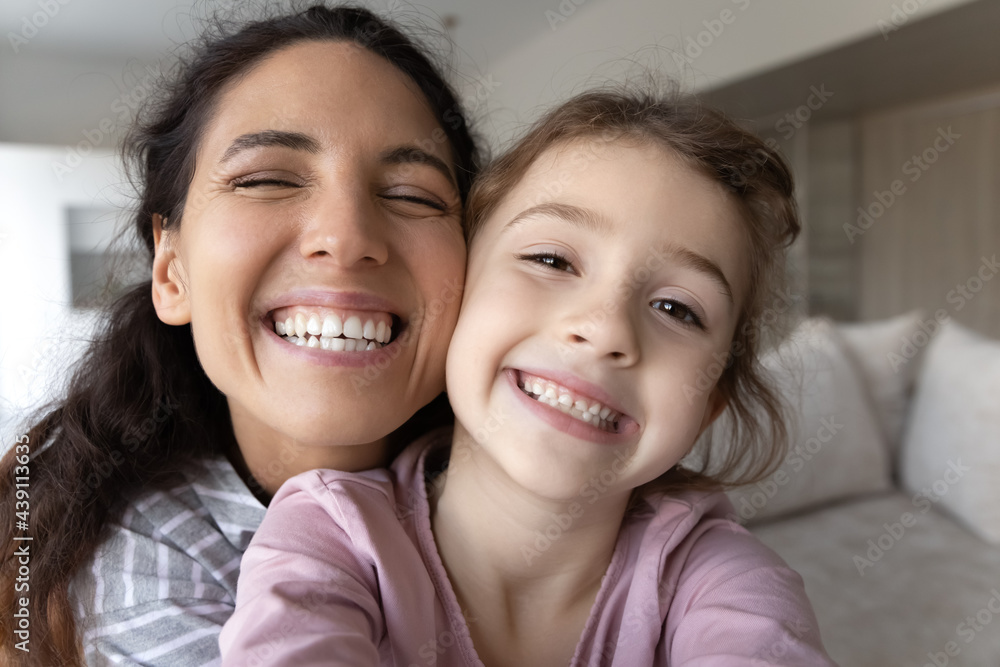 Close up portrait of overjoyed young Latino mother and little biracial daughter make selfie together. Happy Hispanic mom and small ethic girl child take self-portrait picture on camera at home. Close up portrait of overjoyed young Latino mother and little biracial daughter make selfie together. Happy Hispanic mom and small ethic girl child take self-portrait picture on camera at home.