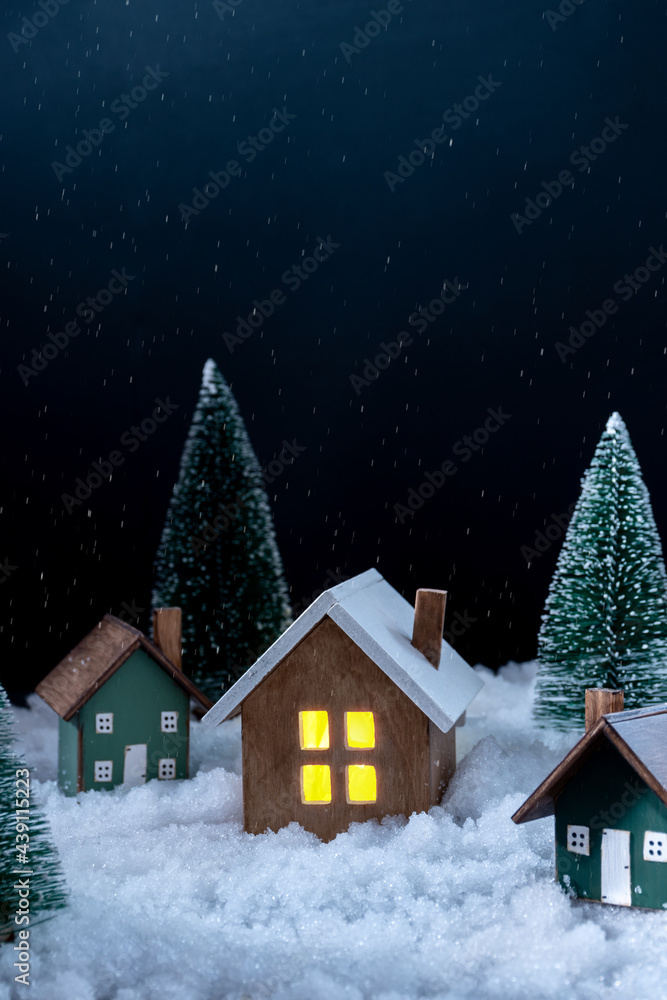 New year and Christmas background. There are artificial  Christmas trees, three figurines of wooden houses and artificial snow on the photography. Copy space. Vertical orientation.