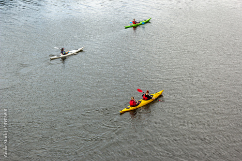 Four people on three kayaks are floating on a calm river. Several people are paddling a kayak. Kayaking on the river. Water active sports. Tourists sailing on kayaks. Single and Double kayak