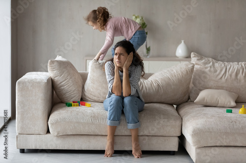 Exhausted Hispanic young mother bothered by loud noise biracial teen daughter playing at home. Tired Latin mom annoyed by ill-behaved naughty kid, suffer from headache. Parenthood concept.