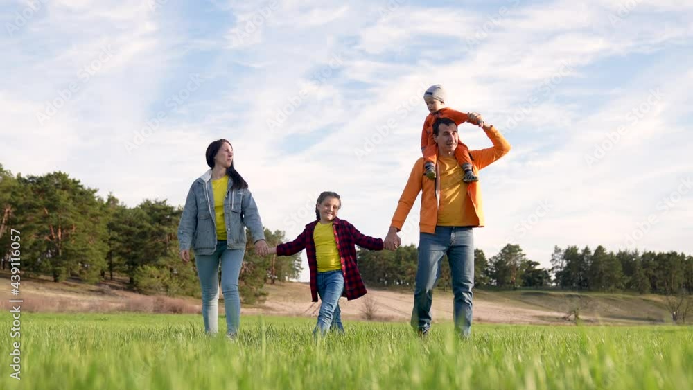 Happy family is walking on green grass. Mom dad and girl with toddler in park at sunset. Happy family walking in park at sunset. Mom dad girl and baby on green grass. Happy family concept at sunset Happy family is walking on green grass. Mom dad and girl with toddler in park at sunset. Happy family walking in park at sunset. Mom dad girl and baby on green grass. Happy family concept at sunset