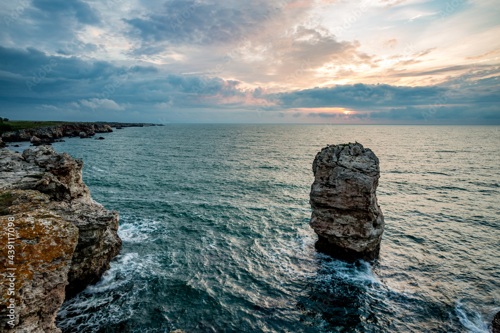 Beautiful cliff standing up in the crystal blue water of Black Sea, near the village of Tyulenovo, Bulgaria. Sunrise landscape capture with impressive dramatic sky.