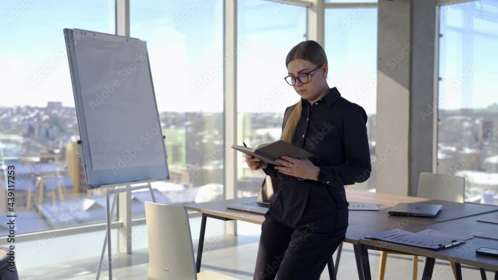 Beautiful business lady in office. Young pretty woman wearing elegant glasses and clothes standing near the table and thinks about new plans in office center. Beautiful business lady in office. Young pretty woman wearing elegant glasses and clothes standing near the table and thinks about new plans in office center.