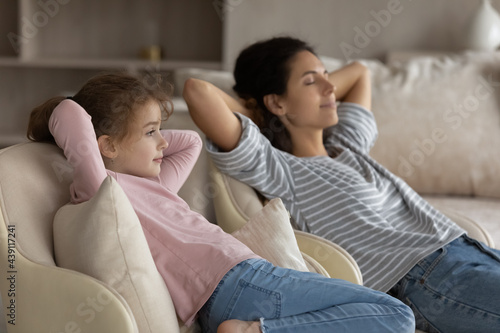Calm happy young Latino mother and little teen daughter relax on sofa in living room relieve negative emotions. Hispanic mom and teenage girl child rest together on couch take nap or sleep.
