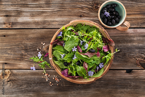 Asian salad mix with baby spinach, mizuna salad, edible flowers and olives on a wooden background, top view, place for text