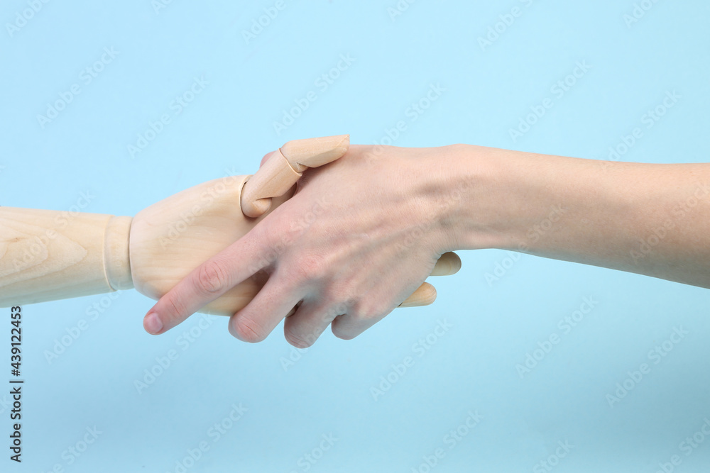 human and wooden hand puppets shake hands on blue background human and wooden hand puppets shake hands on blue background