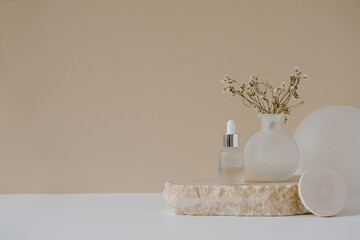 Aesthetic minimalist beauty care therapy concept. Organic serum oil cosmetics bottle on stone with flowers against neutral beige background. Body skin, face treatment product composition