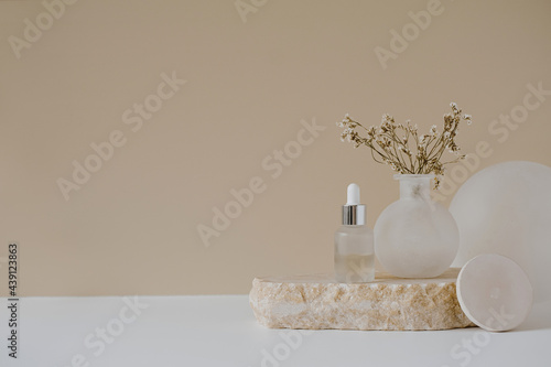 Aesthetic minimalist beauty care therapy concept. Organic serum oil cosmetics bottle on stone with flowers against neutral beige background. Body skin, face treatment product composition photo