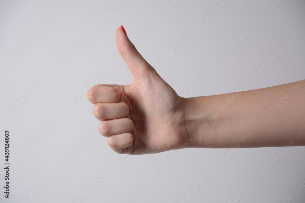 Closeup of female hand showing thumbs up sign against white background.