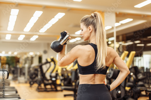 Sexy young fit woman with a perfect body dressed in sportswear trains with a kettlebell in a modern gym. Healthy lifestyle