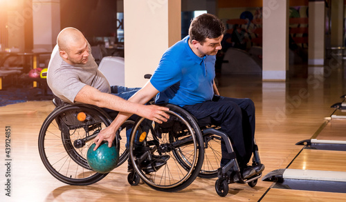 Two young disabled men in wheelchairs playing bowling in the club © romaset