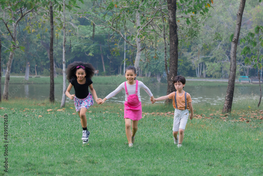 Adorable children hold hand together enjoy running in green park on holiday, group of primary school friendship play in garden, children Afro mix race girl and Asian kids spent time with nature