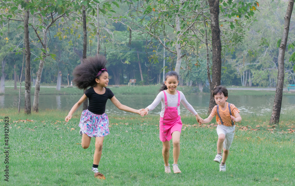 Adorable children hold hand together enjoy running in green park on holiday, group of primary school friendship play in garden, children Afro mix race girl and Asian kids spent time with nature