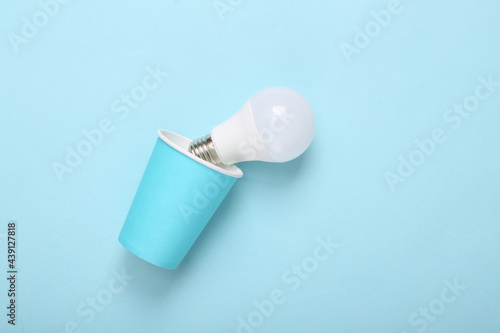 Cardboard cup with light bulb on blue background.