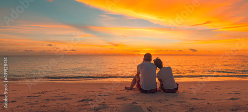 Fototapeta Naklejka Na Ścianę i Meble -  Romantic couple on the beach at colorful sunset on background. Beautiful tropical sunset scenery, romance couple sitting and watching the sunset sea and sky, horizon. Travel, honeymoon destination