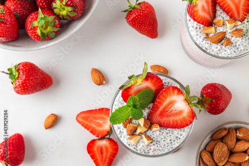 Chia pudding in glasses with fresh strawberries  almonds and mint on white background for vegan breakfast. top view