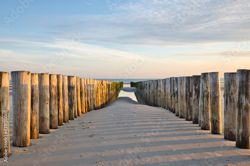 Horizontal view on two rows of pile heads leading towards the North sea at sunset during ebb in summer. Seascape on a sunny day with copy space.