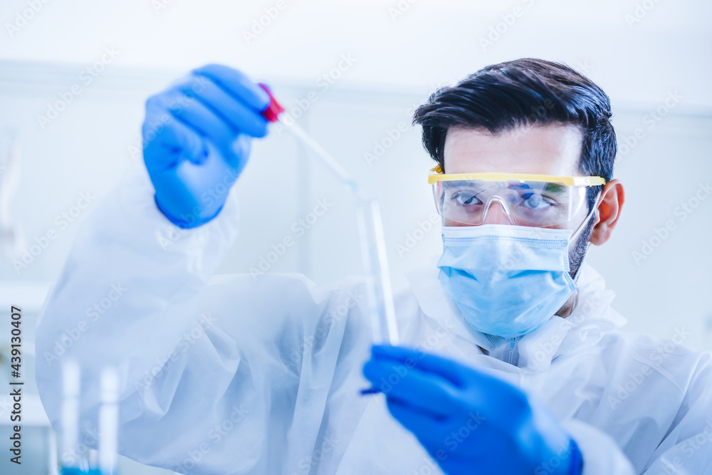 Scientists or doctor using pipette and examining chemical beaker in laboratory. Researcher in protective suit looking at pipette and testing chemical in biotechnological laboratory. Scientists or doctor using pipette and examining chemical beaker in laboratory. Researcher in protective suit looking at pipette and testing chemical in biotechnological laboratory.