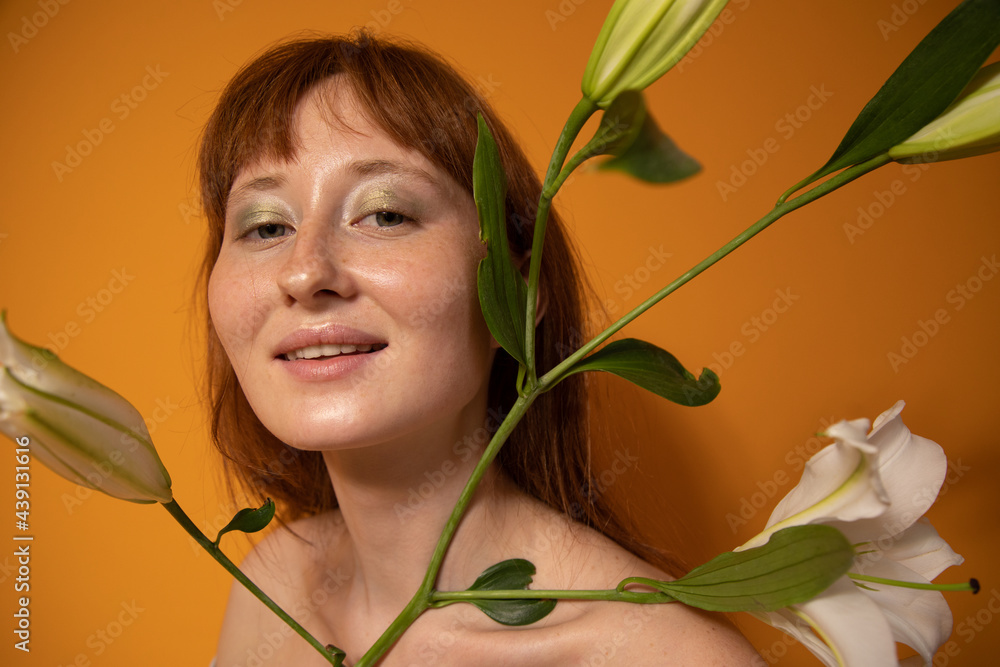 Ginger model with naked shoulders holding lilies and looking at the camera