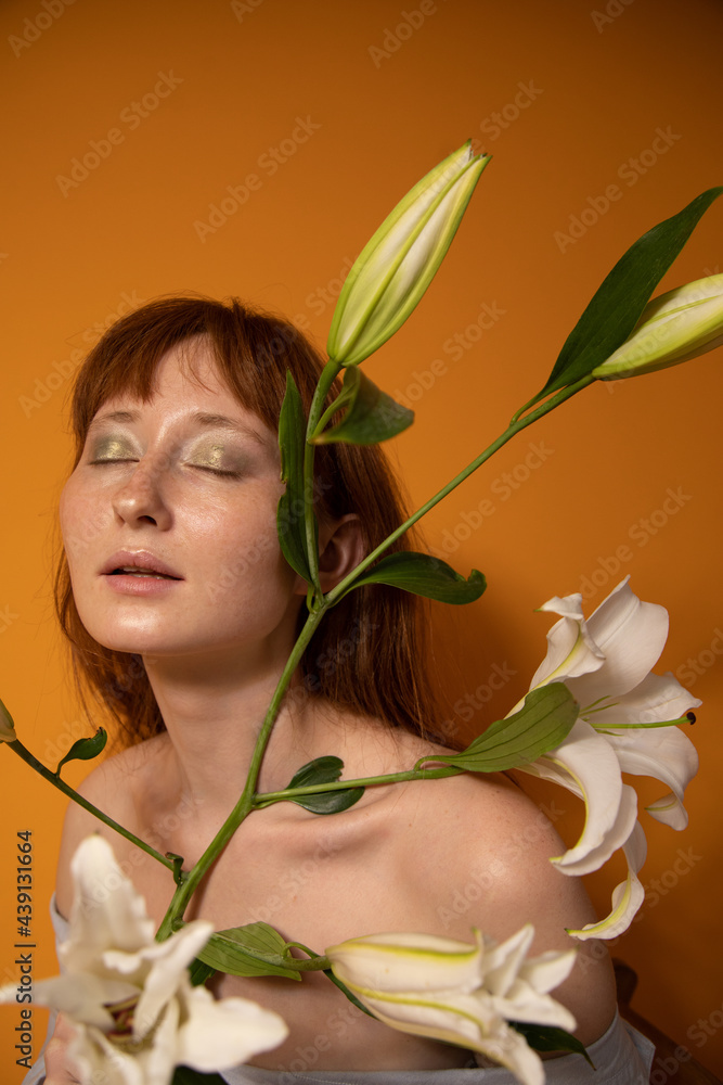 Woman with green eyeshadows closed her eyes and holding lilies while posing