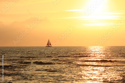 ハワイ島(ビッグアイランド）。一艘のヨットが浮かぶ海に沈む夕日。 © onaka