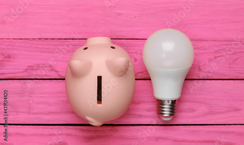 Saving electricity. Led light bulb and piggy bank on pink wooden background. Top view